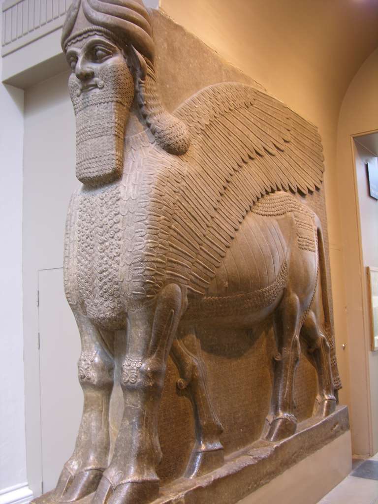 British Museum Top 20 03 Colossal Statue of a Winged Lion 3. Colossal statue of a winged lion - from the palace of Ashurnasirpal II at Nimrud in northern Iraq, about 883-859 BC, 3.5m high by 3.7m wide. Stone mythological guardians, sculpted in relief or in the round, were often placed at gateways to ancient Mesopotamian palaces to protect them from demonic forces. This winged lion has five legs so that when viewed from the front it is standing firm, and when viewed from the side it appears to be striding forward against any evil. It wears ropes like other protective spirits.